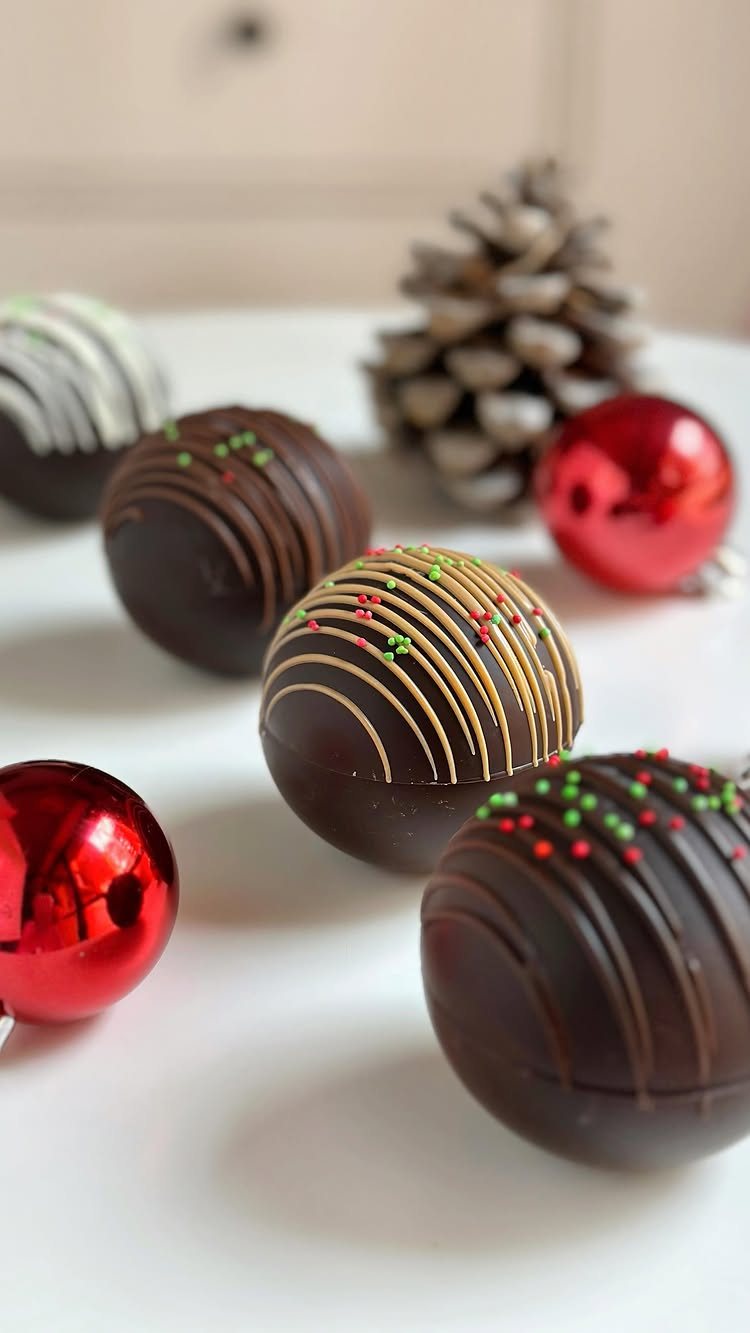 12 Hot Chocolate Bombs for Every Holiday and Skill Level 2 Chocolate spheres decorated with colorful sprinkles and thin chocolate drizzles on a white surface.