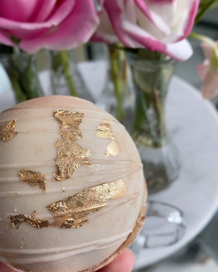 12 Hot Chocolate Bombs for Every Holiday and Skill Level 6 A decorated hot chocolate bomb with white chocolate swirls and gold leaf flakes held in a hand.