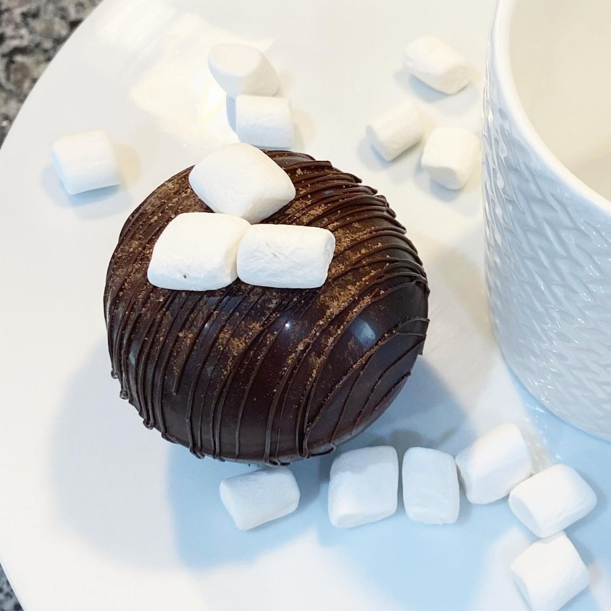 12 Hot Chocolate Bombs for Every Holiday and Skill Level 7 A chocolate hot chocolate bomb topped with mini marshmallows on a white plate.