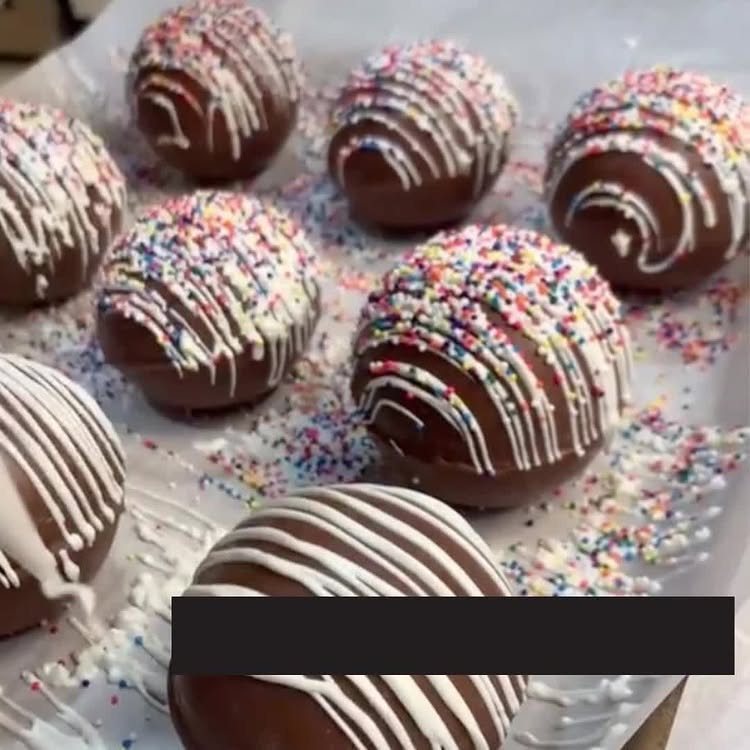 12 Hot Chocolate Bombs for Every Holiday and Skill Level 11 Chocolate spheres decorated with white chocolate drizzle and colorful sprinkles on a white surface.