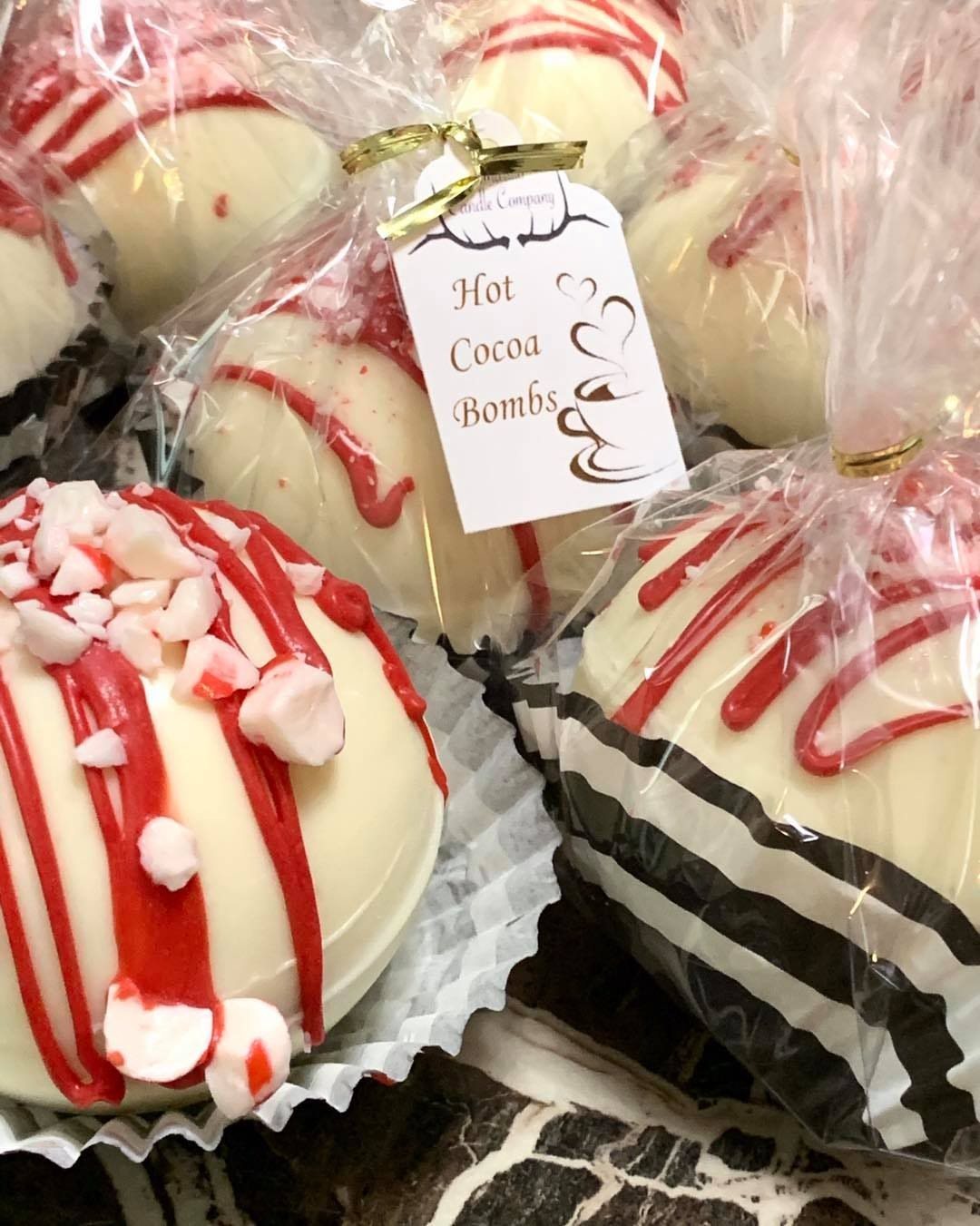 12 Hot Chocolate Bombs for Every Holiday and Skill Level 5 White chocolate cocoa bombs with red drizzle and pink candy pieces wrapped in clear cellophane.