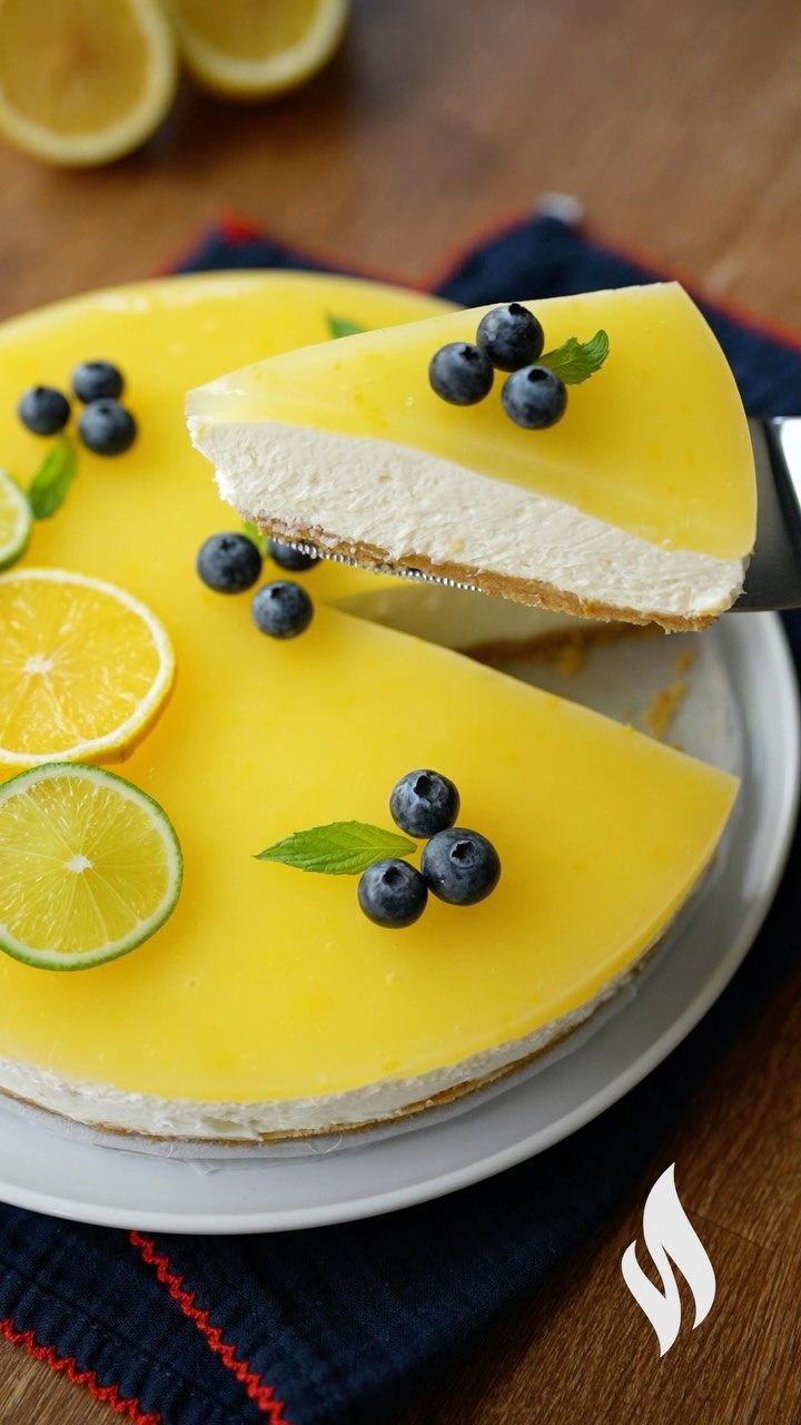 A slice of lemon cheesecake with blueberries and mint being lifted from a whole cake.