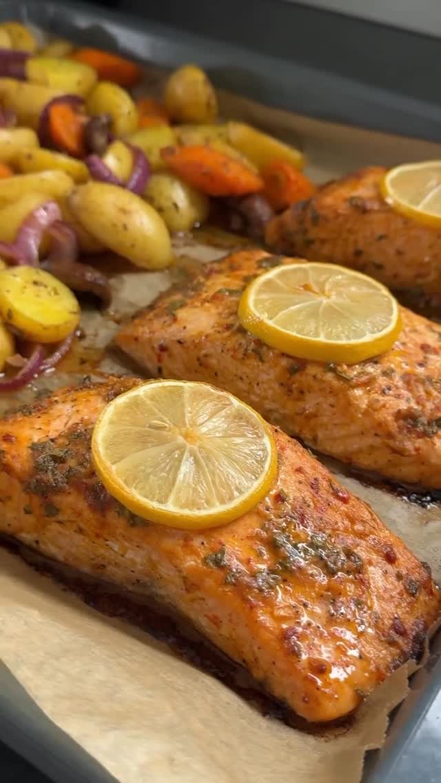 Cooked salmon fillets topped with lemon slices and herbs on a baking sheet with roasted vegetables.