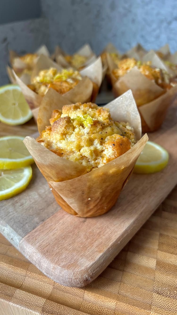 Lemon muffins in paper liners on a wooden board with fresh lemon slices.