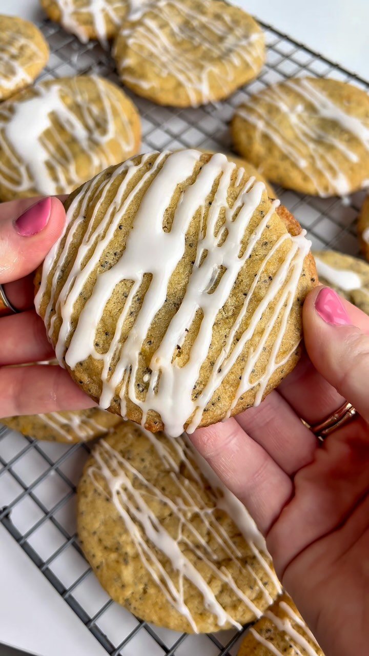 Hands holding a single lemon cookie drizzled with white icing over a cooling rack.