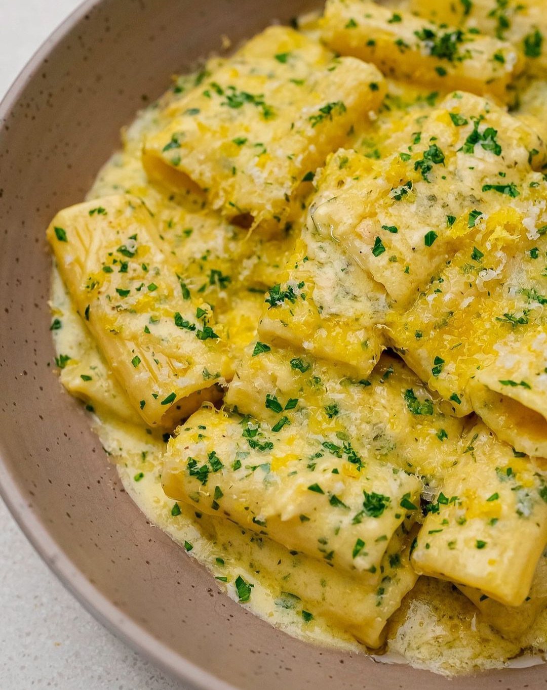 Rigatoni pasta in a creamy lemon sauce garnished with parsley and zest in a bowl.