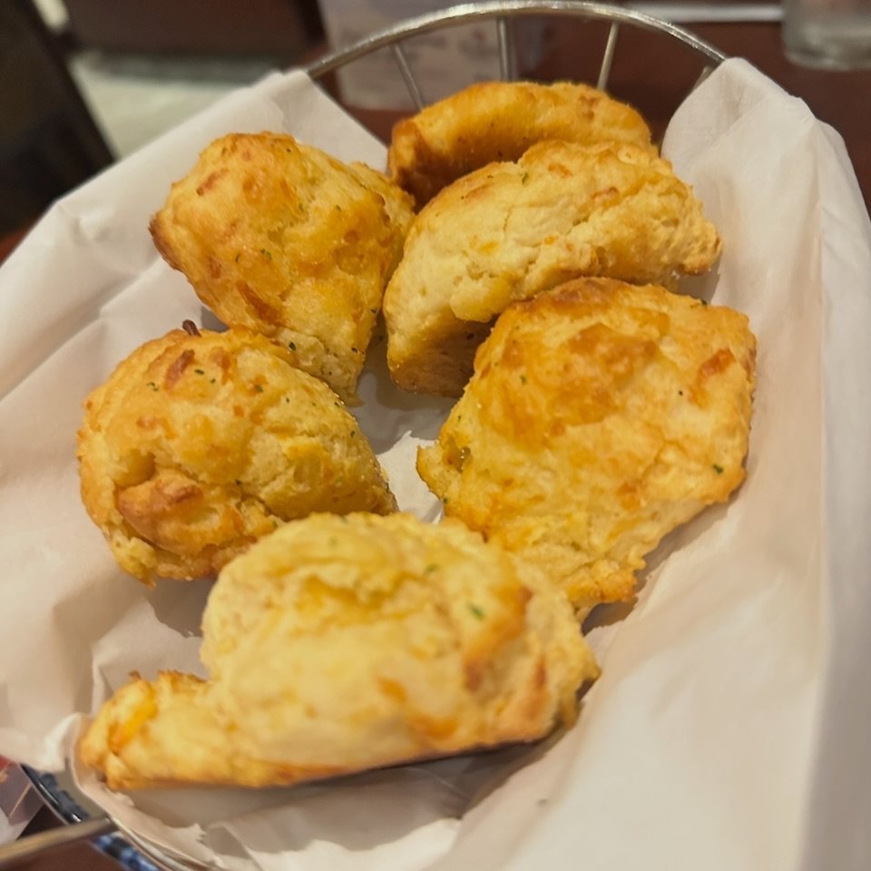 Golden brown cheddar biscuits served in a wire basket lined with white parchment paper.