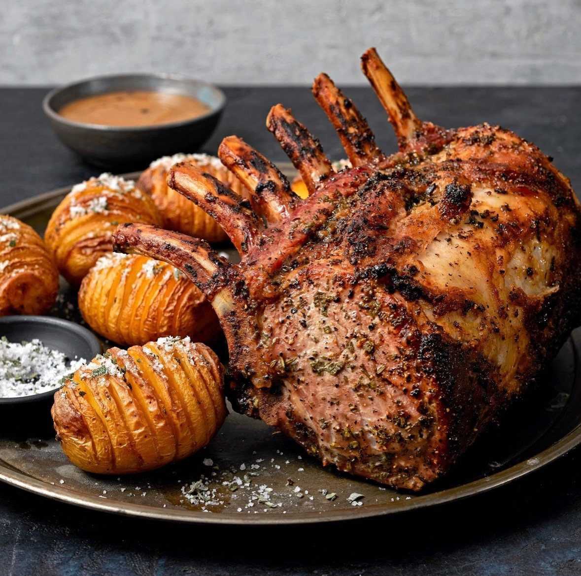 Roasted prime rib and sliced Hasselback potatoes on a dark platter with gravy.