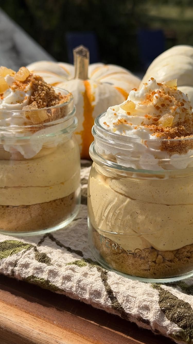 Two glass jars filled with layered pumpkin pudding topped with whipped cream and crumbs.