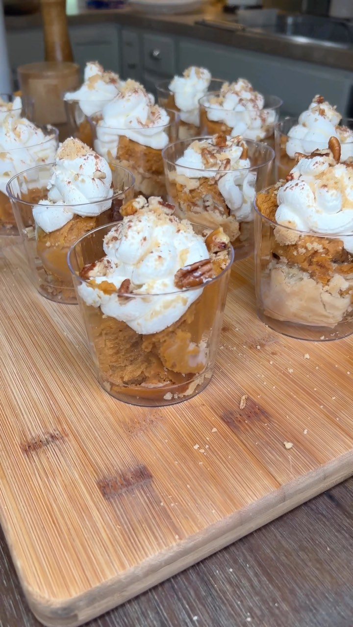 Small clear cups filled with pumpkin pudding and whipped cream topped with nuts on a wooden board.
