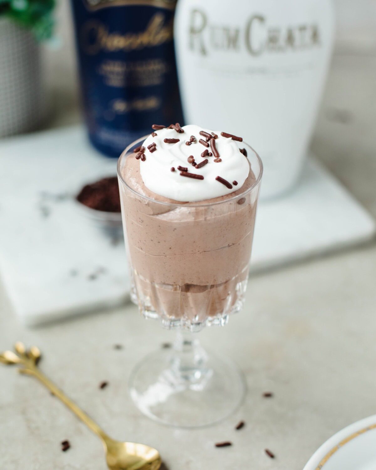 Chocolate pudding shot in a glass goblet topped with whipped cream and chocolate sprinkles on marble.