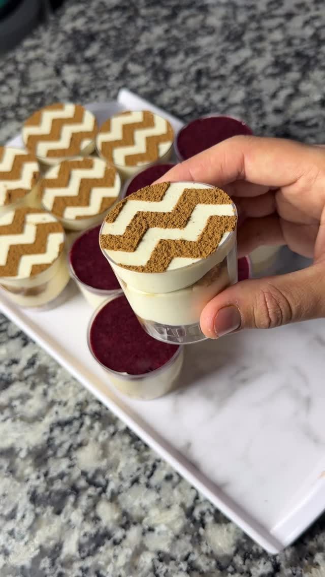 A hand holding a small shot glass filled with white pudding and a brown chevron pattern.