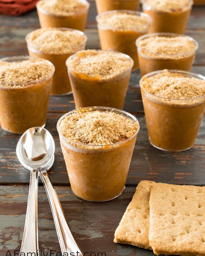 Small glasses of pumpkin pudding topped with graham cracker crumbs on a dark wooden table.