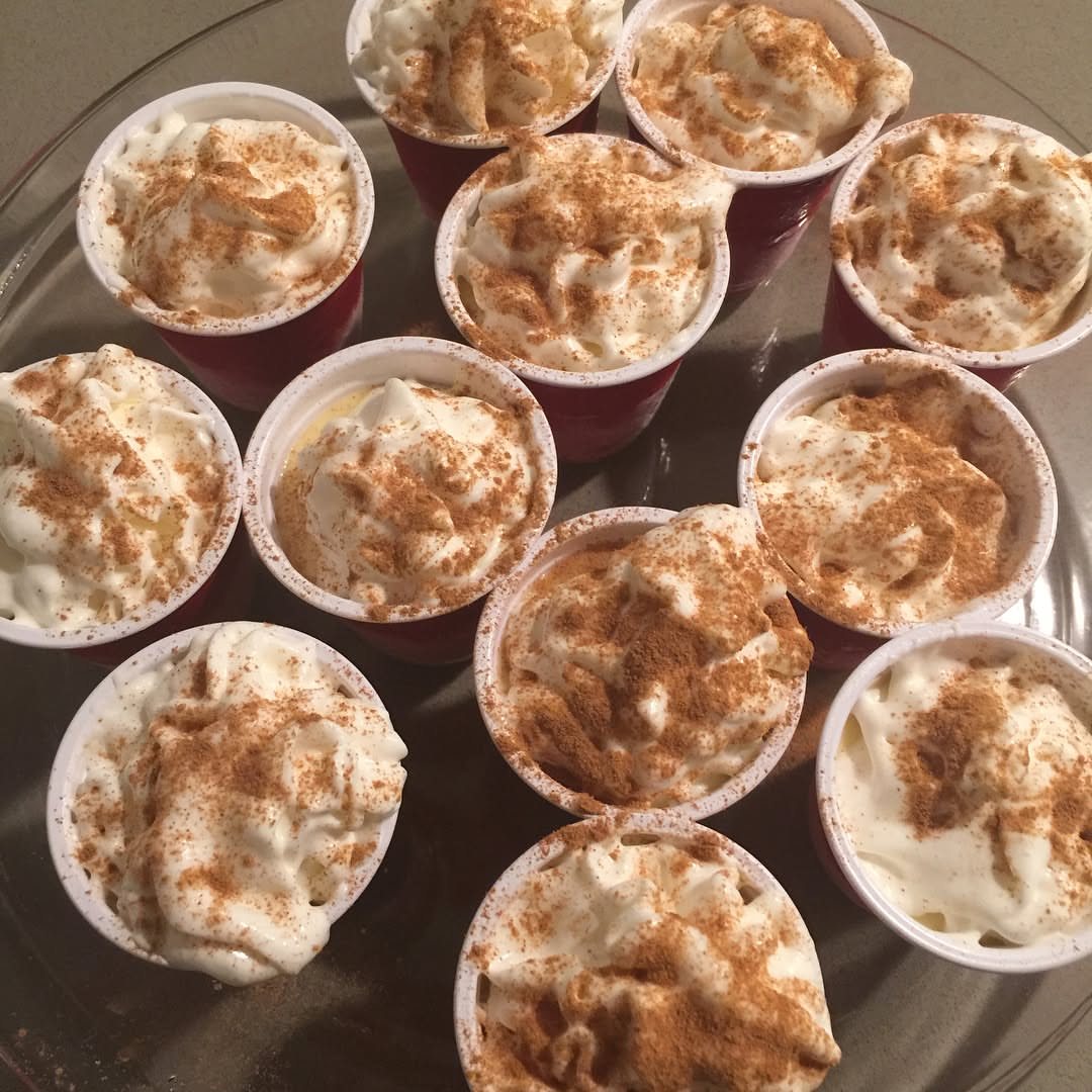 Small white shot cups filled with creamy pudding and whipped cream topped with cinnamon powder.