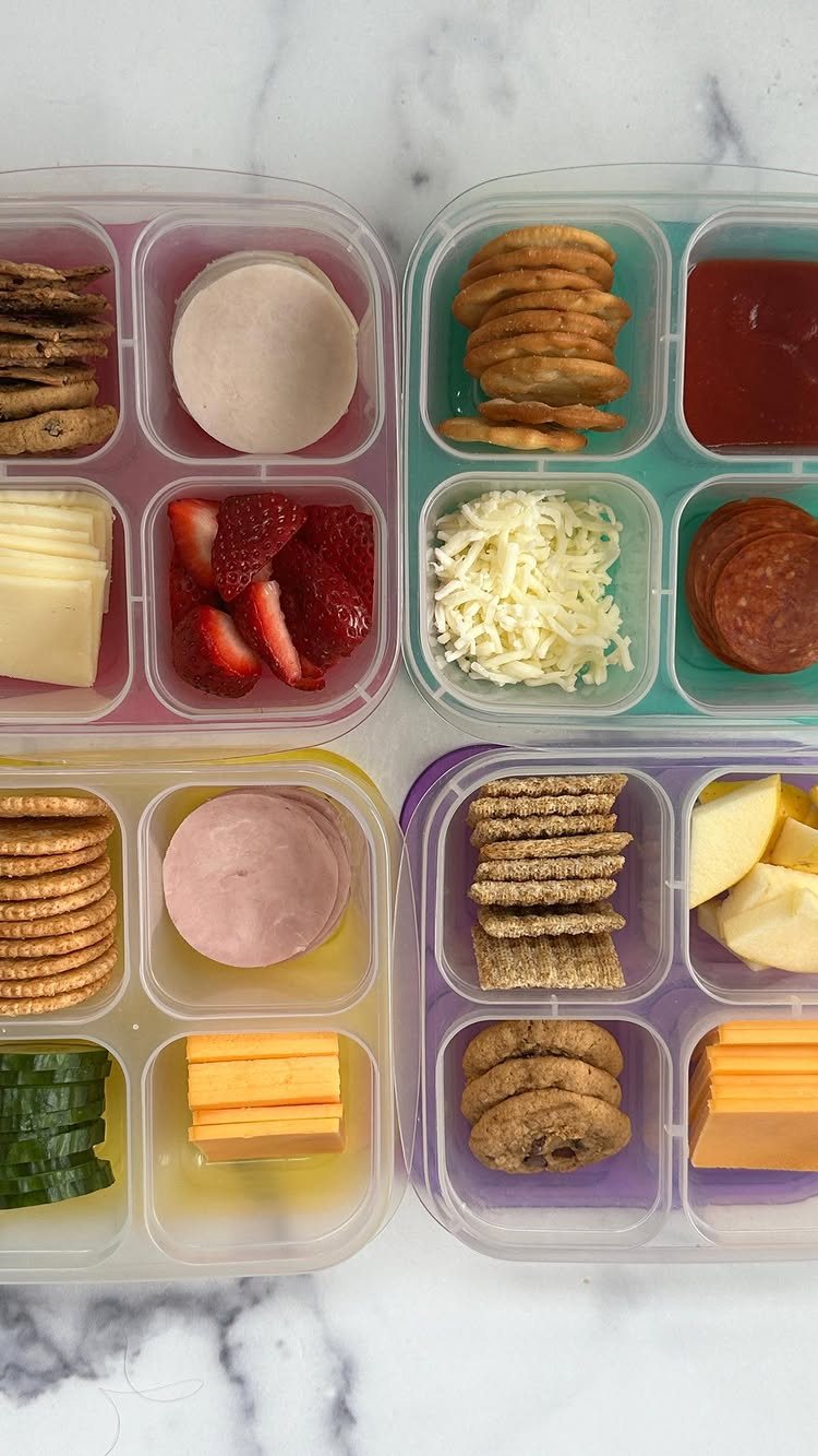 19 School Lunch Ideas for Real Mornings 15 Four bento boxes filled with crackers, cheese, strawberries, and pepperoni on a marble background.