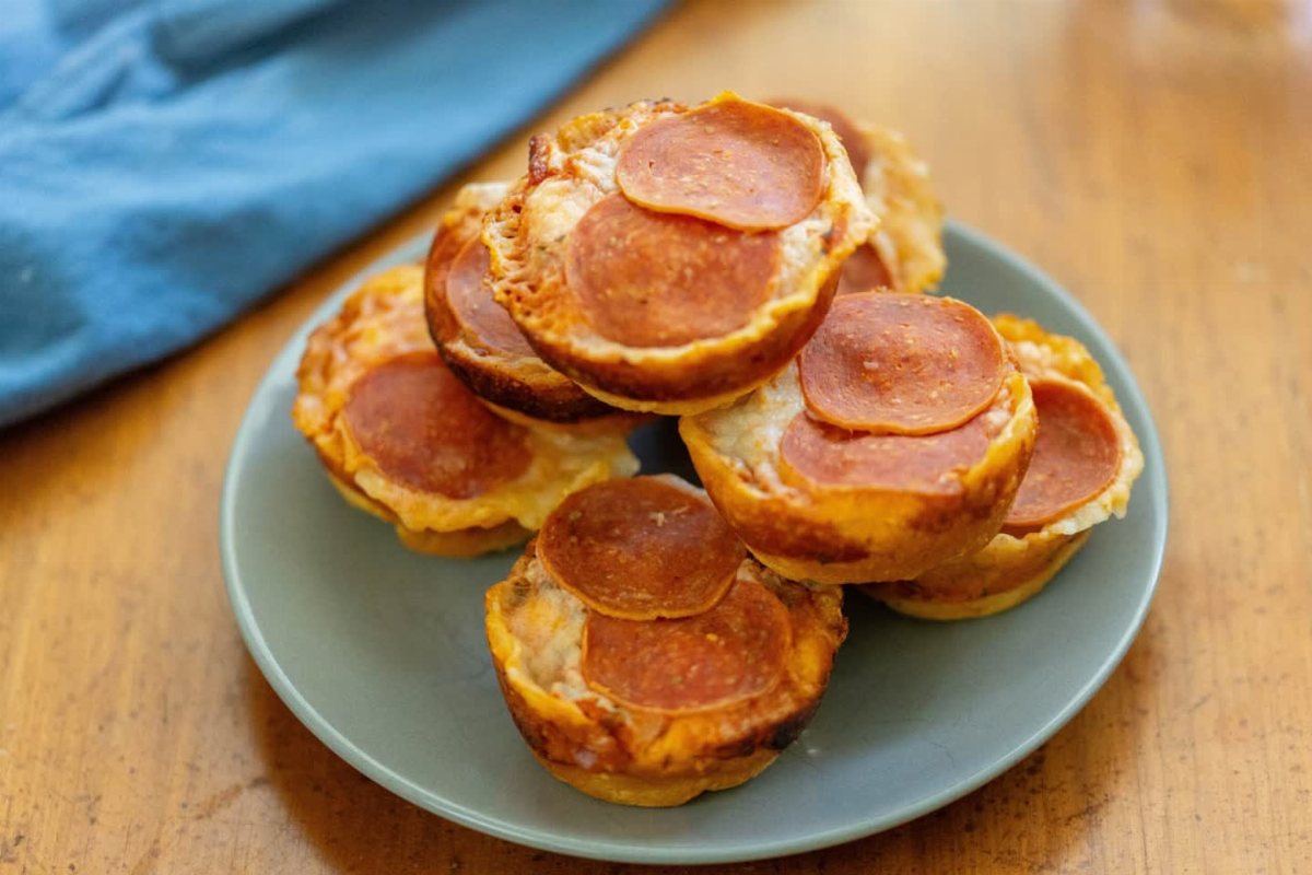 19 School Lunch Ideas for Real Mornings 9 Small pepperoni pizza muffins stacked on a light blue plate on a wooden table.