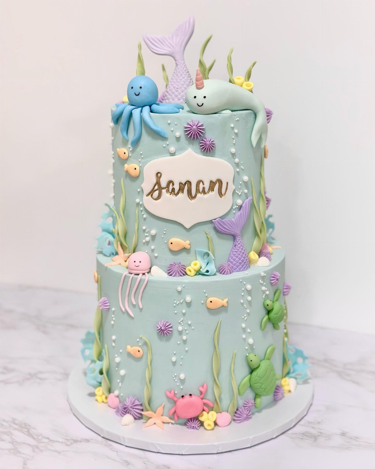 8 Undersea Cake Ideas From Fondant Reefs to Jellyfish Buttercream 1 Two-tier light blue cake decorated with colorful fondant sea creatures and pastel coral decorations.