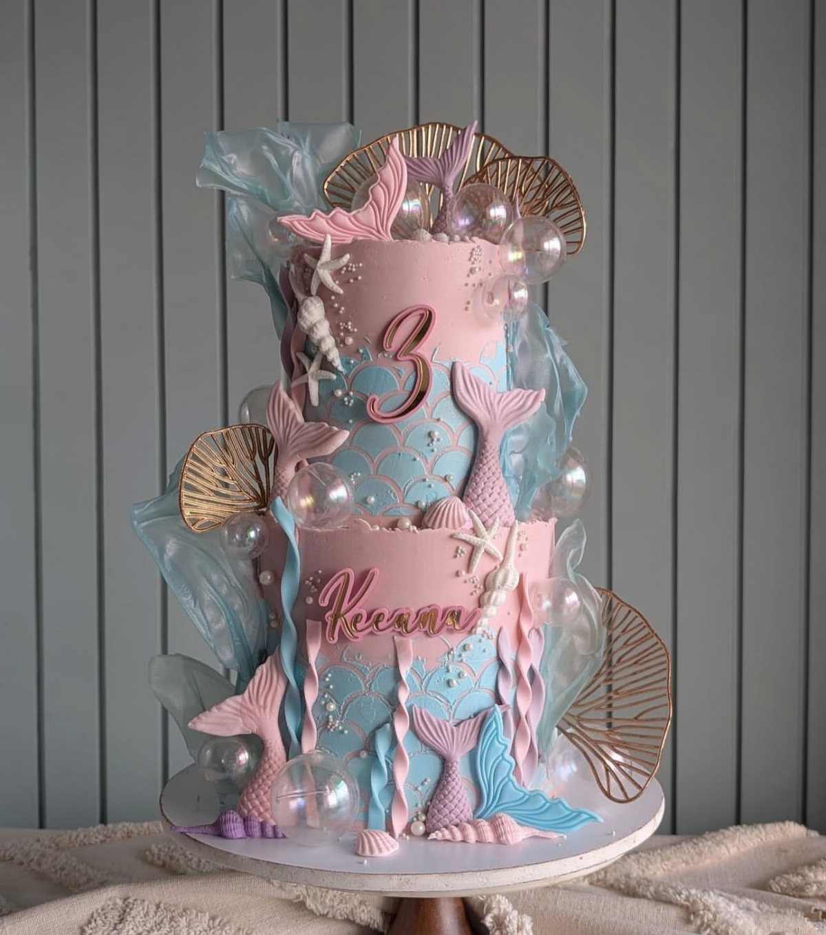 8 Undersea Cake Ideas From Fondant Reefs to Jellyfish Buttercream 2 Two-tier pink and blue mermaid themed cake decorated with tails, shells, and pearls.
