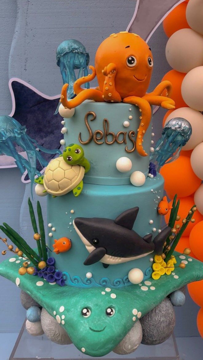 8 Undersea Cake Ideas From Fondant Reefs to Jellyfish Buttercream 3 A blue tiered undersea cake featuring an orange octopus, a sea turtle, and a shark.
