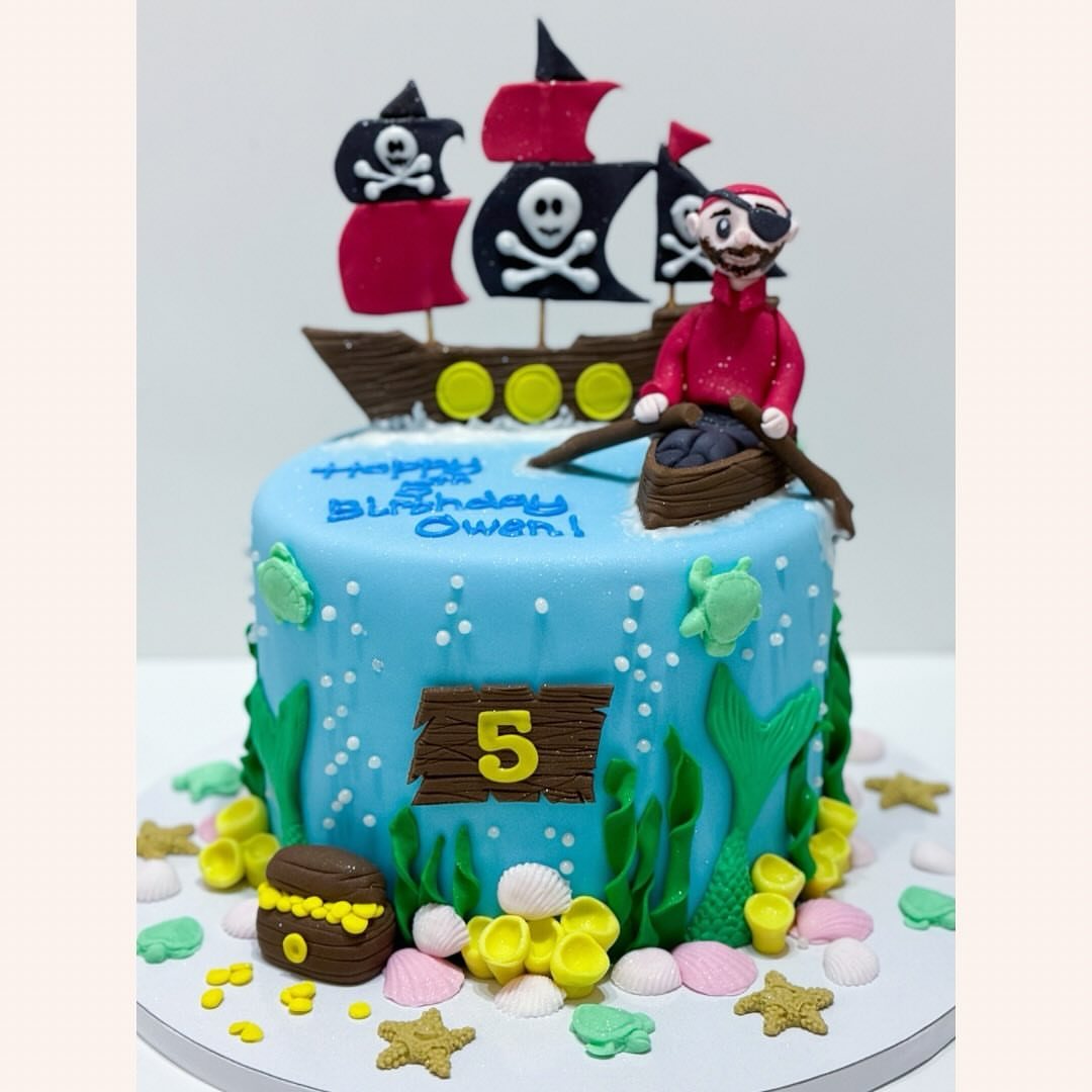 8 Undersea Cake Ideas From Fondant Reefs to Jellyfish Buttercream 6 A blue pirate-themed birthday cake decorated with seaweed, seashells, and a pirate ship topper.