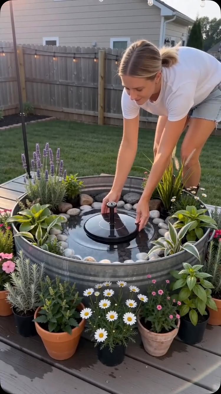 10 Backyard Fountain Ideas for Patios, Walls & Small Spaces 10 A woman setting up a DIY fountain inside a large metal tub surrounded by potted plants.