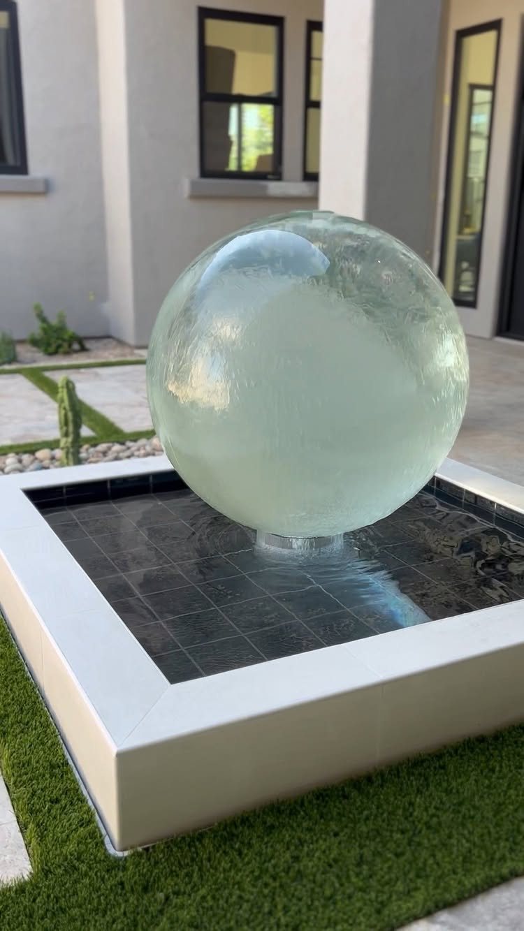 10 Backyard Fountain Ideas for Patios, Walls & Small Spaces 7 A large translucent glass sphere fountain flowing with water in a modern outdoor courtyard.