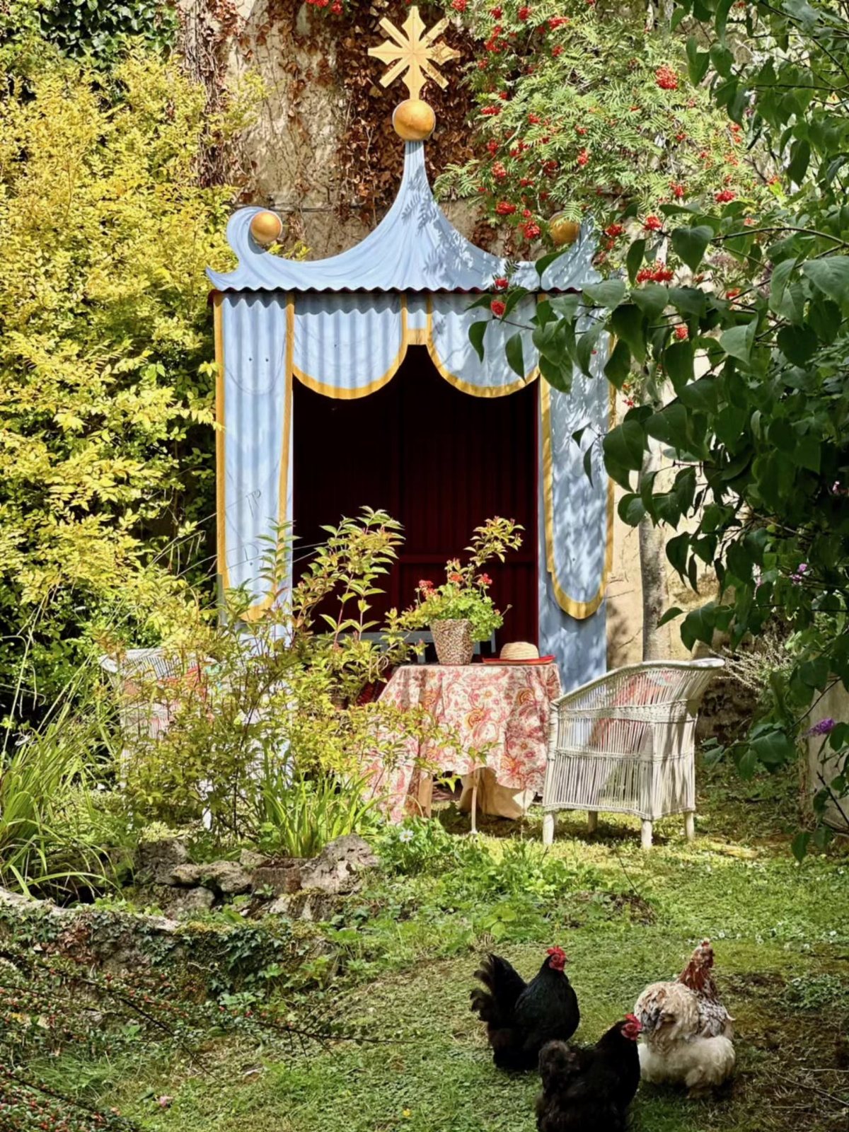 17 English Garden Ideas: Roses, Paths & Cozy Details 11 A decorative blue garden structure with gold accents sits amidst lush greenery and chickens.