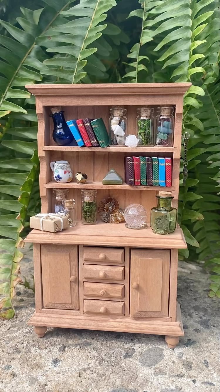 13 Fairy Garden Ideas: Broken Pots to Teacup Worlds 4 Miniature wooden bookshelf filled with tiny books and small glass jars among green ferns.