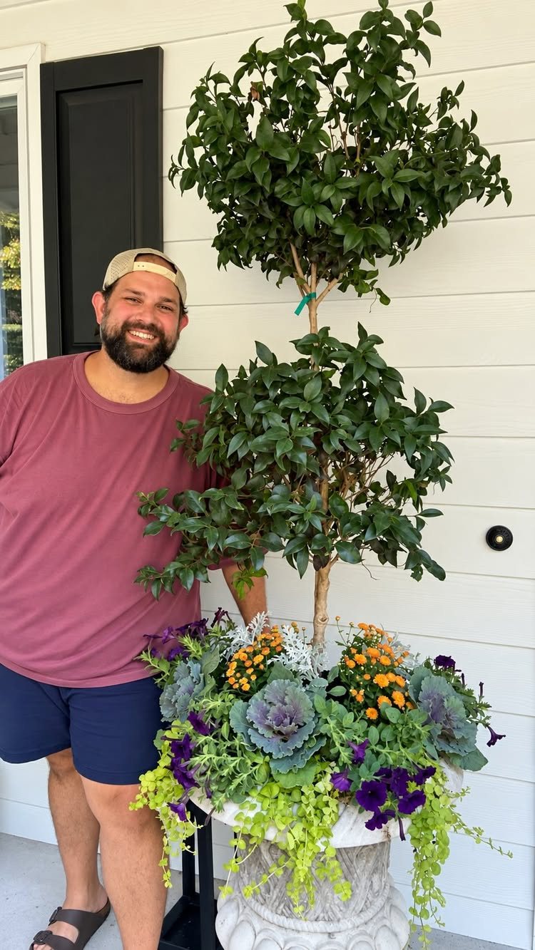 Fall Planter Ideas: 12 Container Combos for Color, Foliage and Texture 5 A man standing beside a large white urn filled with colorful fall plants and a tall topiary.