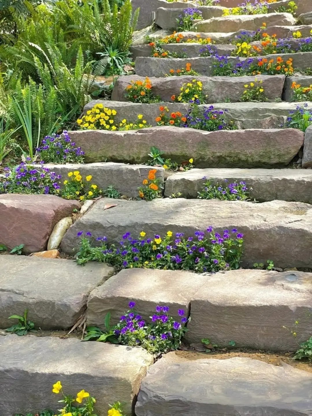 19 Flower Bed Ideas for Every Corner of the Yard 18 Stone steps with colorful small flowers growing in the crevices between the large rocks.