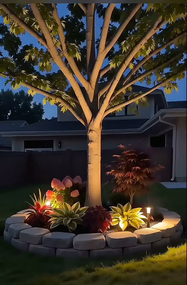 20 Flower Garden Ideas for Every Corner of Your Property 10 A circular stone-edged garden bed with colorful plants surrounding the base of a large tree.