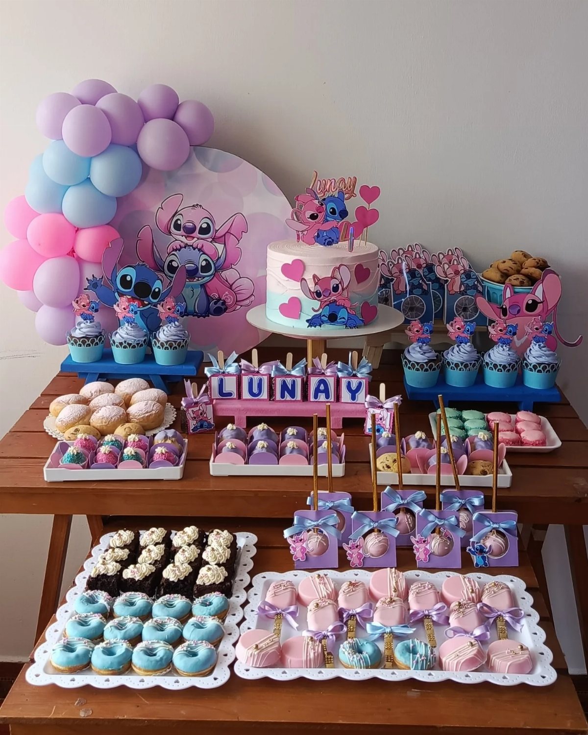 Stitch themed dessert table with cake, cupcakes, donuts, and colorful treats on a wooden table.