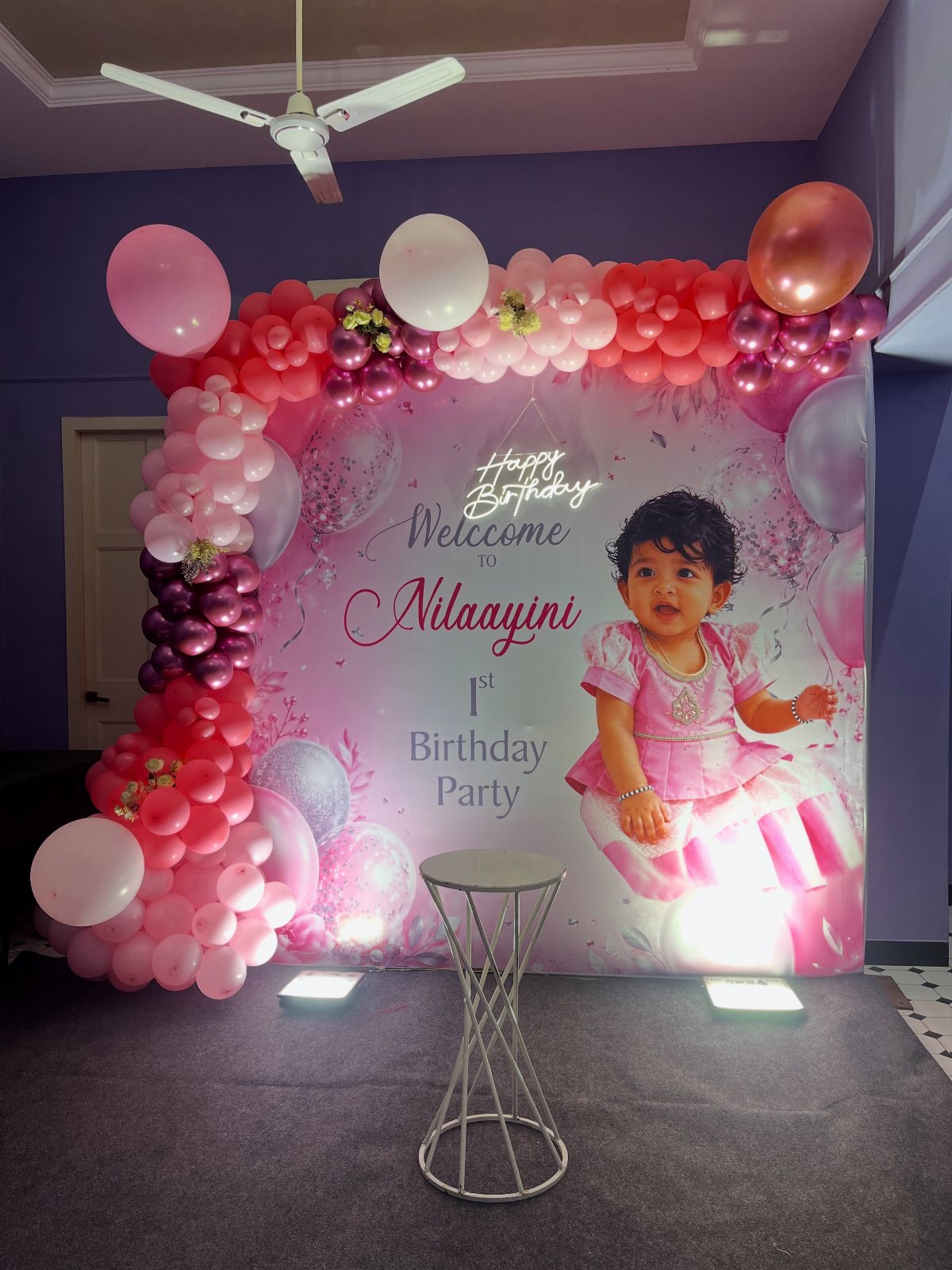 Pink and white balloon arch framing a personalized birthday backdrop with a child's photo.