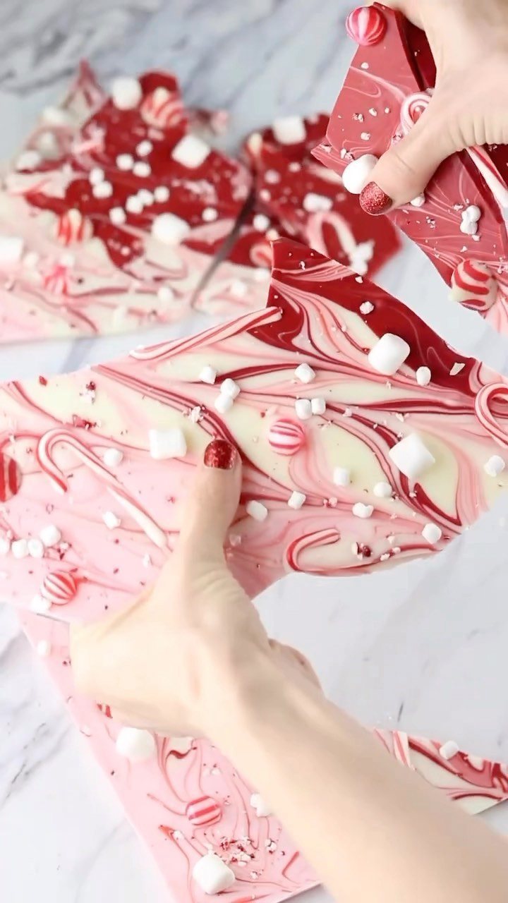 Candy Cane Themed Party: 9 Ideas for Decor and Desserts 8 Hands holding pieces of red and white peppermint bark decorated with marshmallows and candy cane bits.