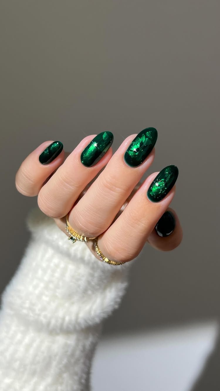 22 Christmas Nail Designs Ideas for 2026 Holiday Manicures 13 Hand with long emerald green glittery nails and gold rings wearing a white sweater.