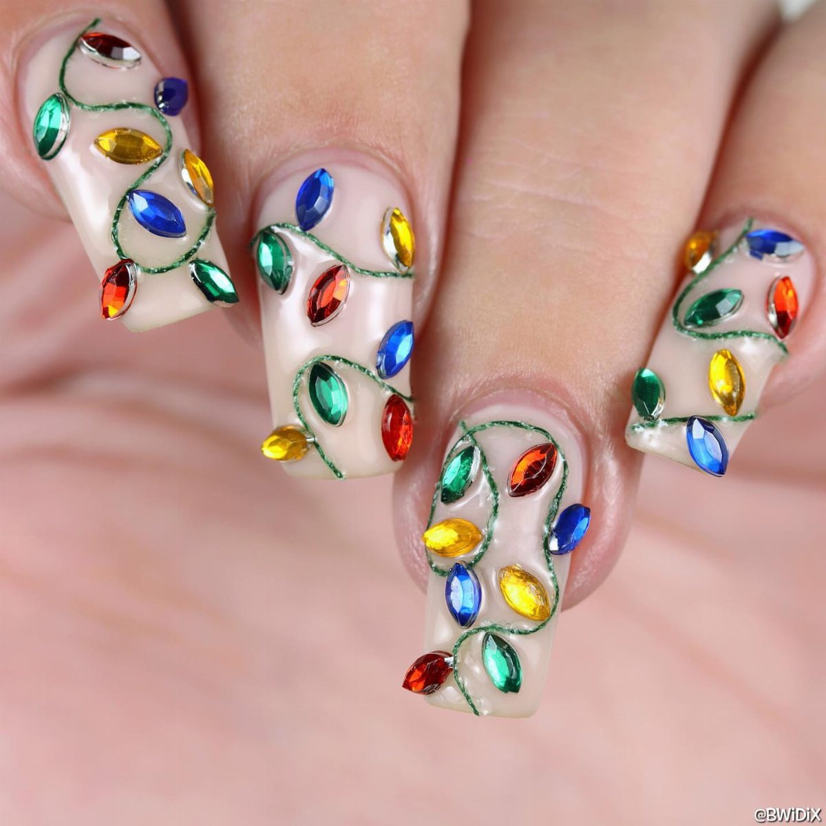 22 Christmas Nail Designs Ideas for 2026 Holiday Manicures 10 Long coffin-shaped nails decorated with colorful jewel-like gems and green swirling lines resembling Christmas lights.