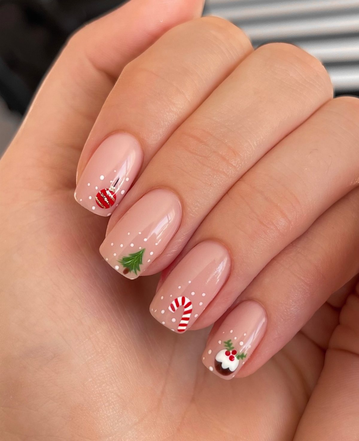 22 Christmas Nail Designs Ideas for 2026 Holiday Manicures 12 Manicured hand showing nude nails with small Christmas designs like candy canes and trees.