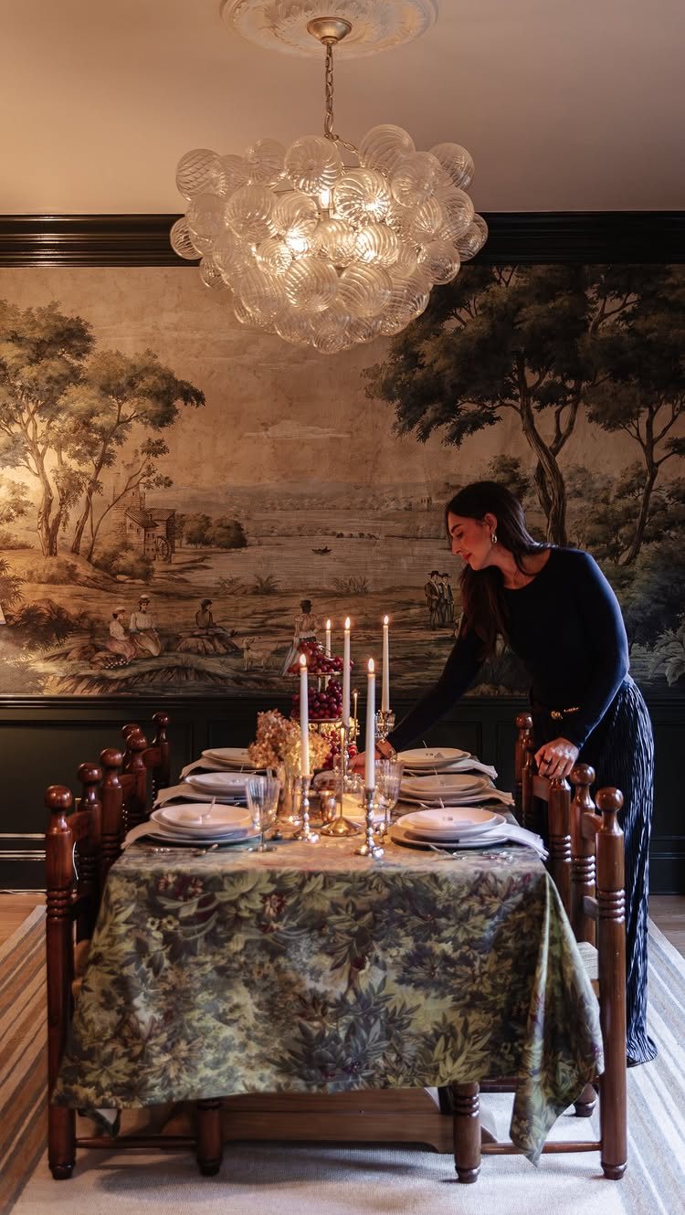 Christmas Table Place Setting Ideas: 16 Styles to Try 3 A woman arranging layered white plates and tall taper candles on a patterned green tablecloth.