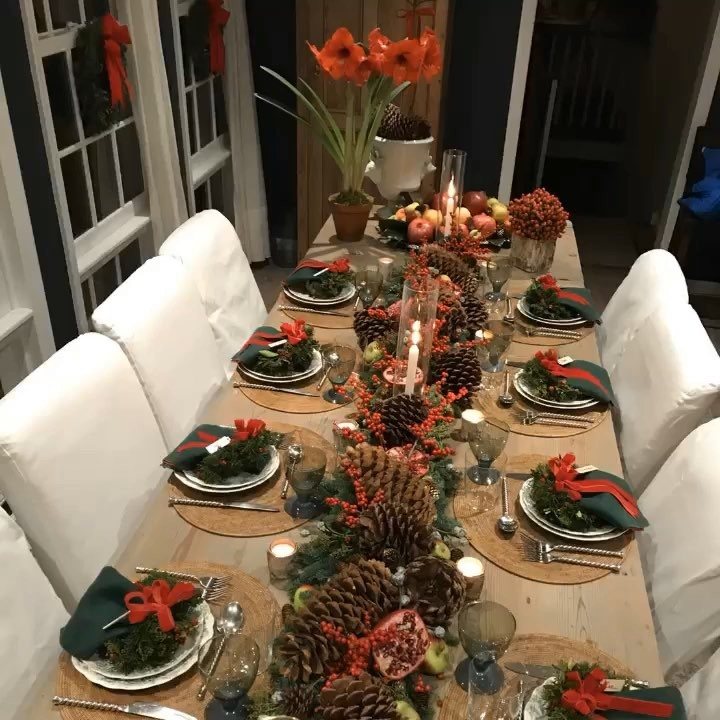 Christmas Table Place Setting Ideas: 16 Styles to Try 2 A long wooden dining table decorated with pinecones, berries, and festive place settings for a holiday meal.