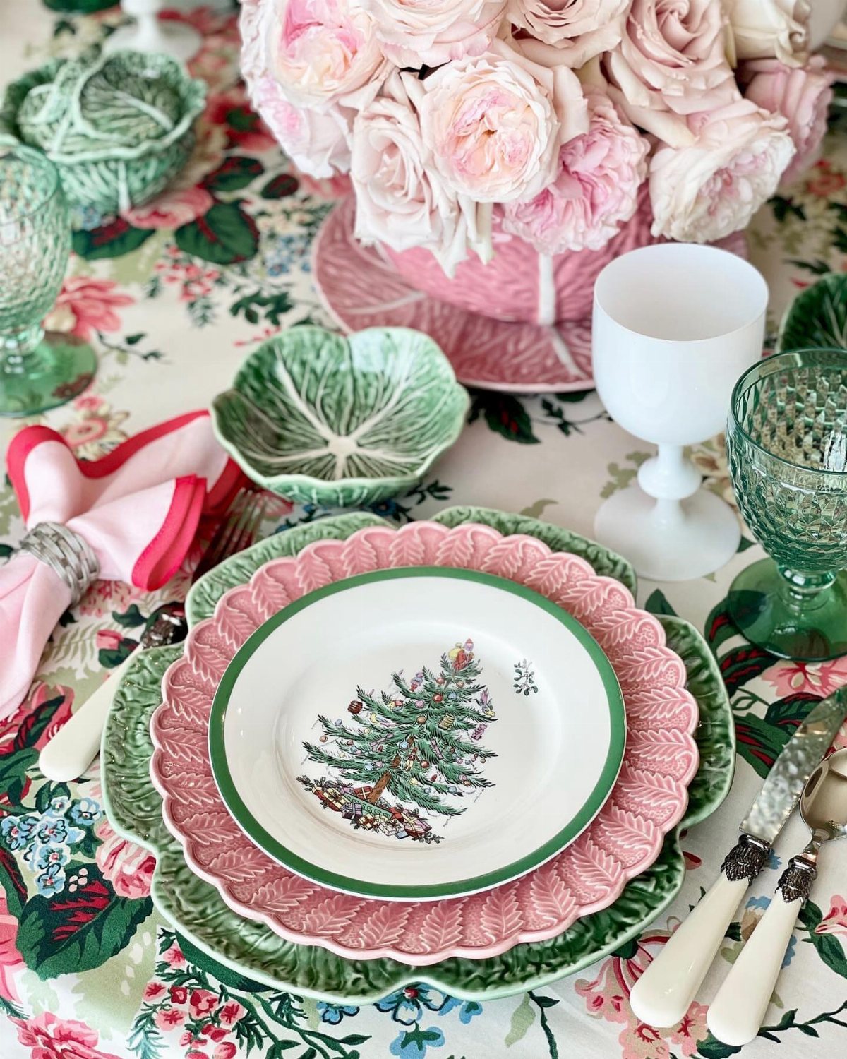 Christmas Table Place Setting Ideas: 16 Styles to Try 1 Layered scalloped plates in pink and green with a Christmas tree design on a floral tablecloth.
