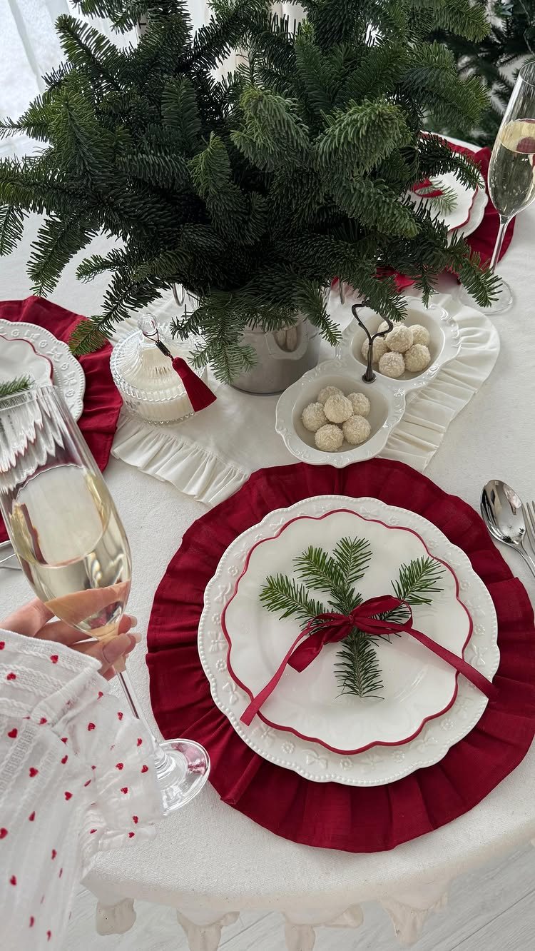 Christmas Table Place Setting Ideas: 16 Styles to Try 12 A festive Christmas place setting with a red ruffled charger, white scalloped plate, and an evergreen sprig tied with red ribbon.