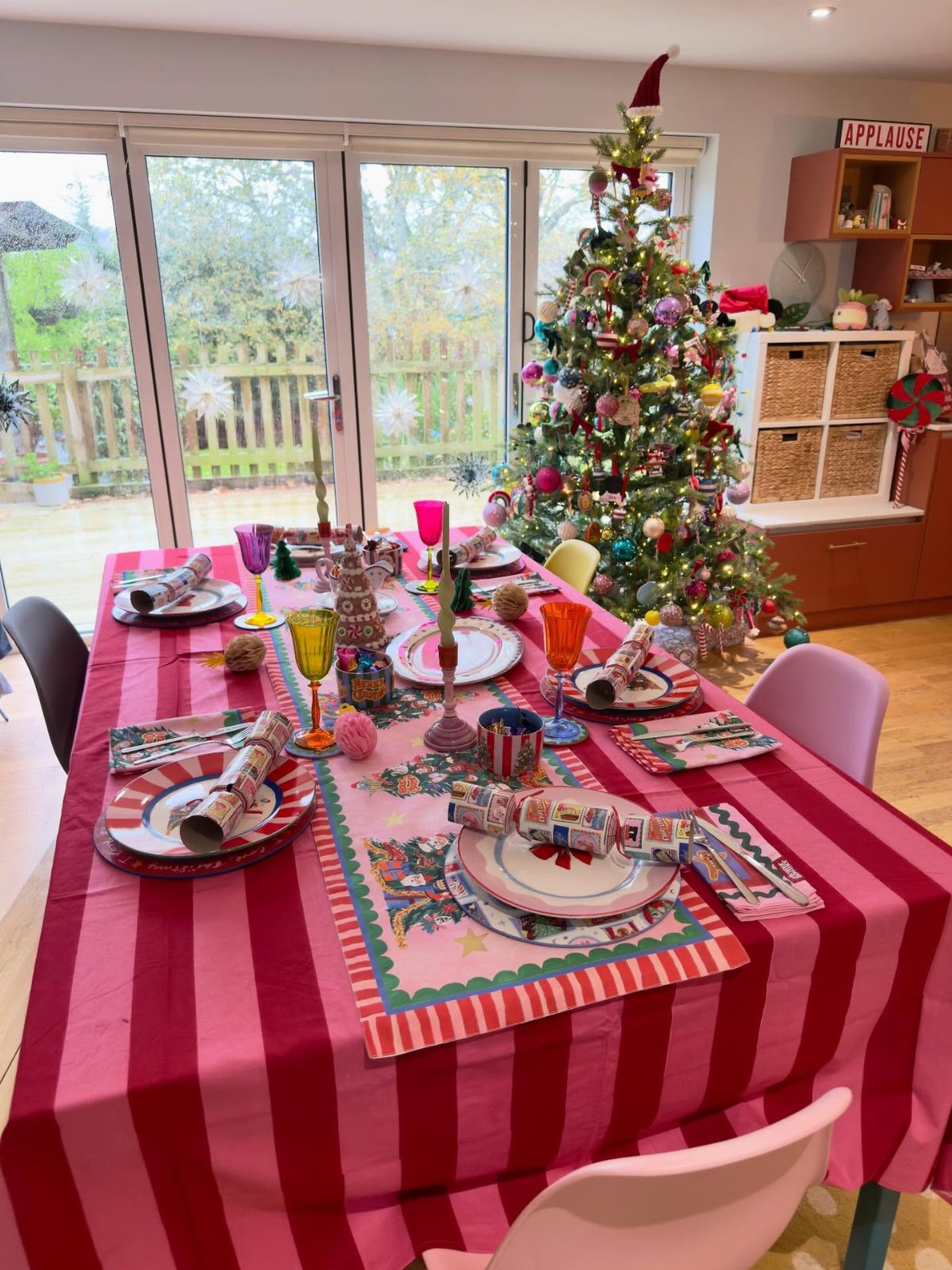 Christmas Table Place Setting Ideas: 16 Styles to Try 15 A festive Christmas table setting with colorful plates, glassware, and crackers on a striped tablecloth.