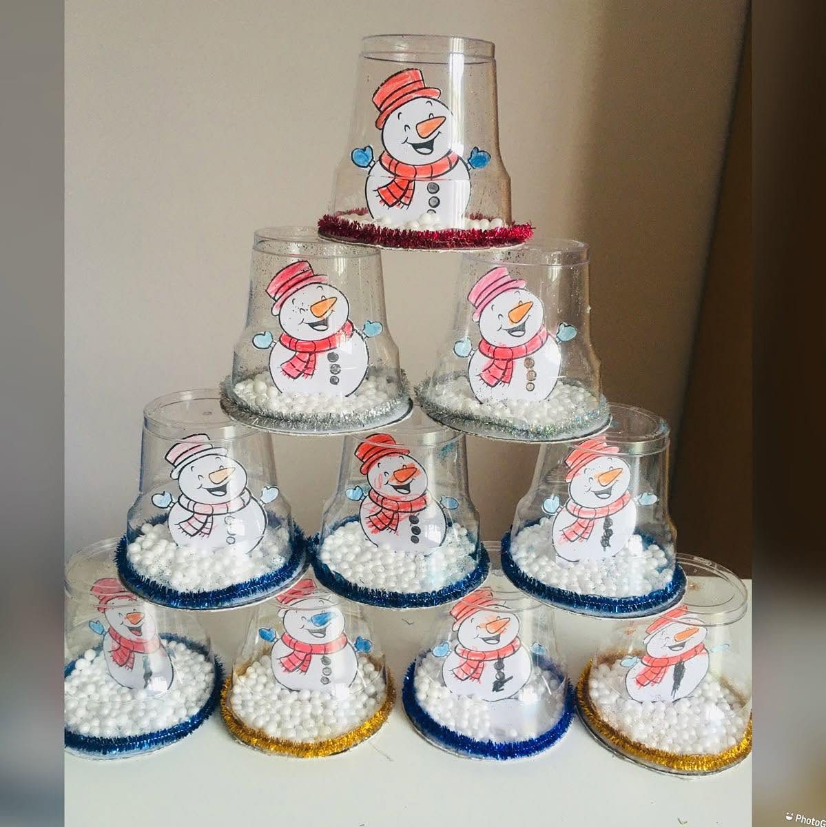 A pyramid of clear plastic cups filled with faux snow and snowman illustrations decorated with glitter.