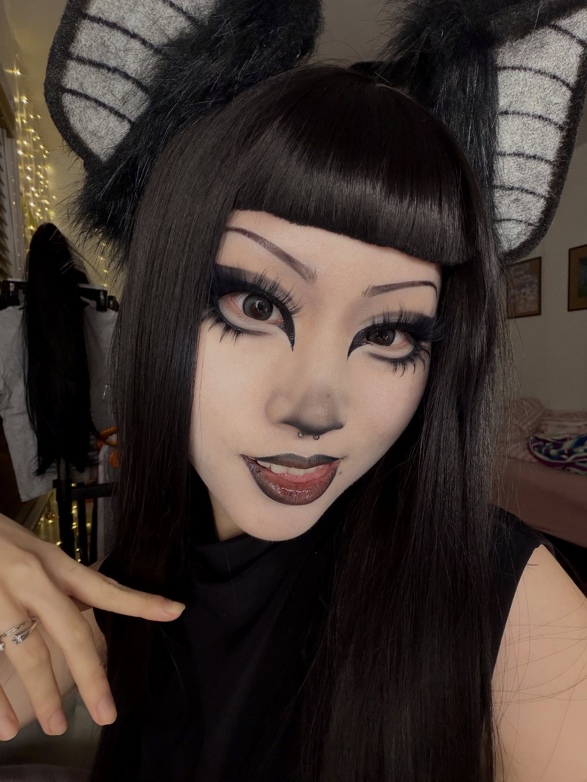 Person with pale white face makeup, heavy black eyeliner, and large black cat ears.