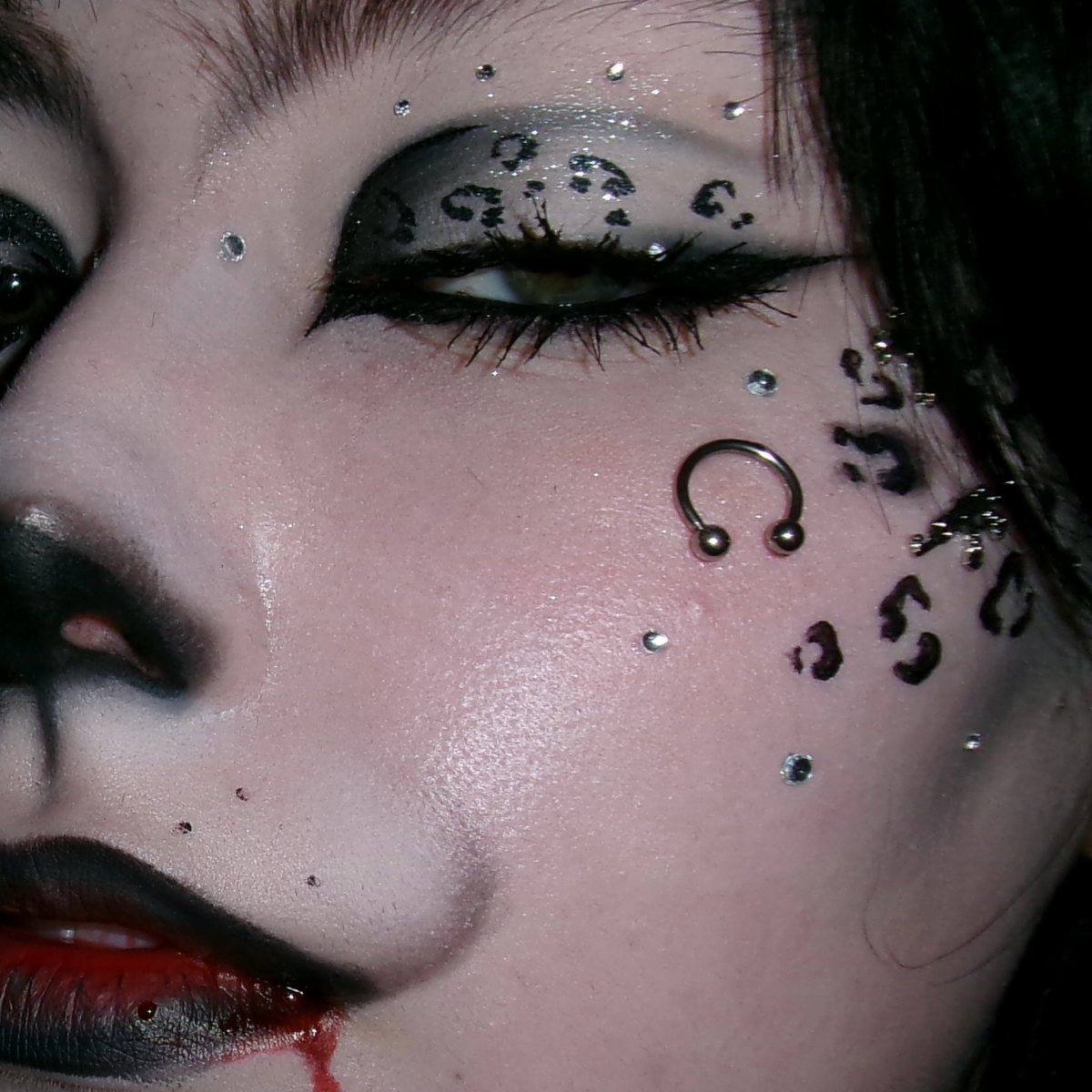 Person with dark smoky eye makeup featuring leopard print patterns and silver rhinestones.