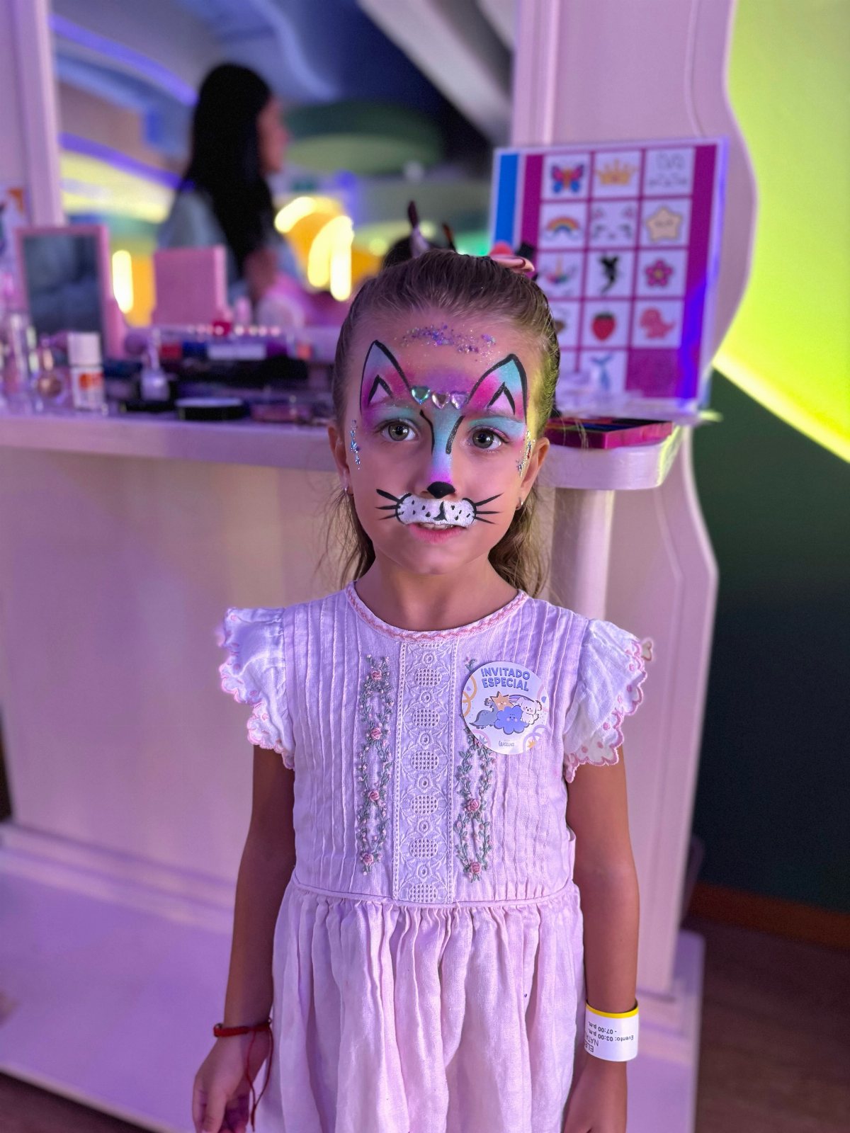 Young girl with pink and white cat face paint and whiskers looking at the camera.