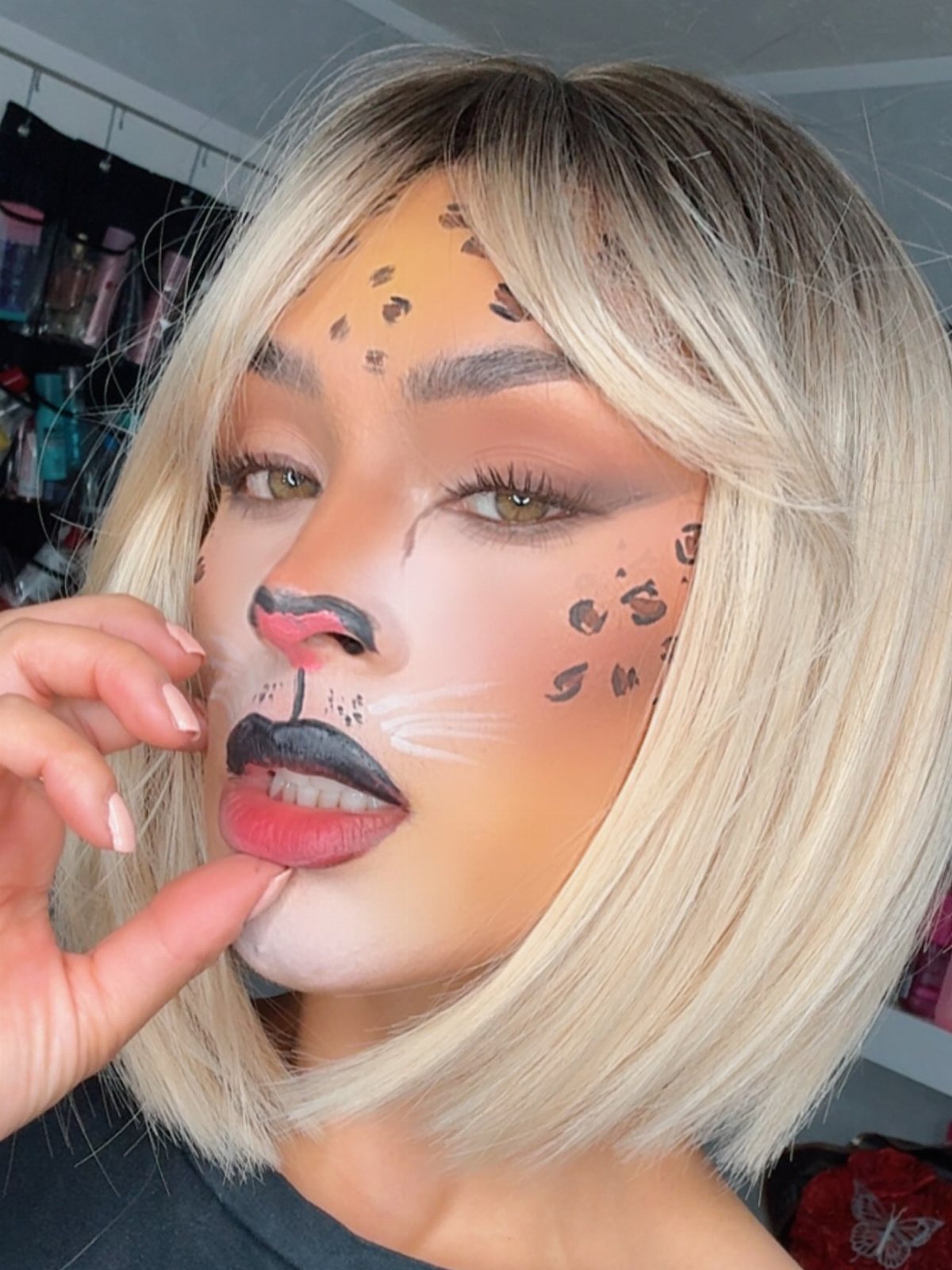 Person with blonde hair wearing leopard print face makeup and white whiskers.
