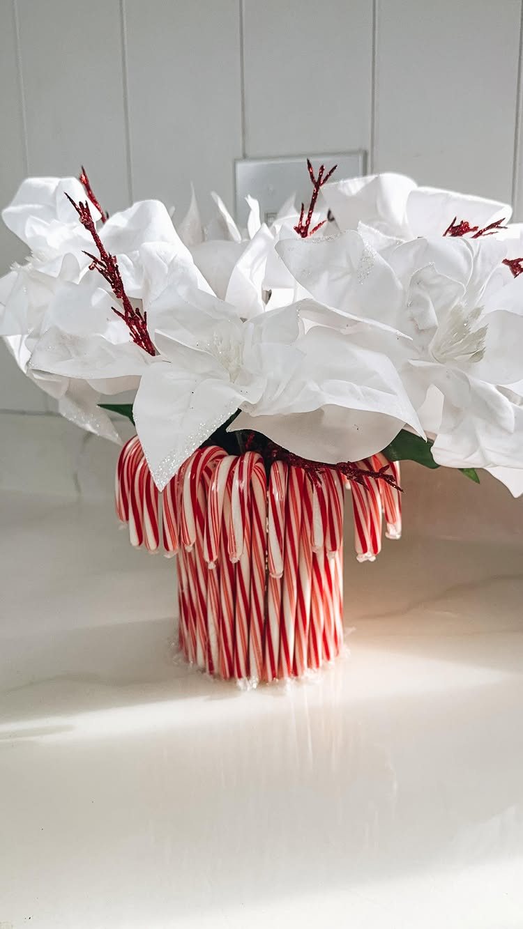 14 Decorating Cheap for Christmas Ideas for 2026 9 White poinsettia flowers arranged in a vase decorated with red and white candy canes.