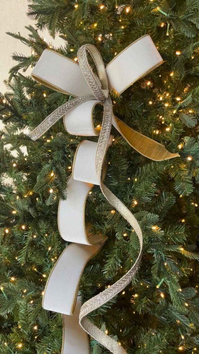 14 Decorating Cheap for Christmas Ideas for 2026 3 A large white and silver glittered ribbon bow decorating a lit green Christmas tree.