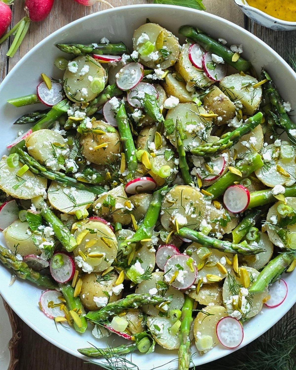 Potato salad with green asparagus, sliced radishes, and crumbled cheese in a white bowl.